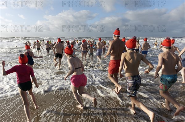 Many people in swimwear and Christmas hats run into the cold sea in winter