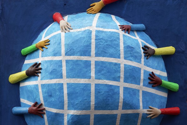 Hands with different skin colours reaching for a globe made of papier-mache