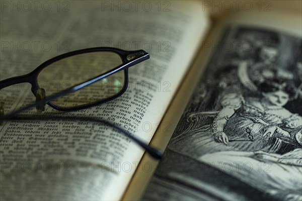 Opened old book with illustration and glasses