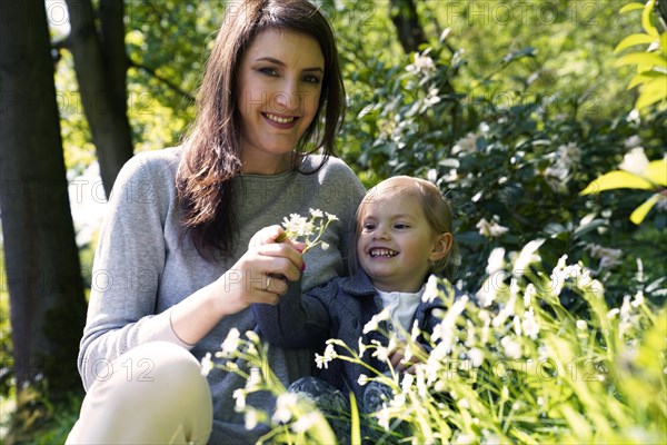 Mother sits with little daughter in flower meadow