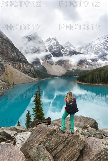 Young woman standing in front of a lake looking into mountain scenery