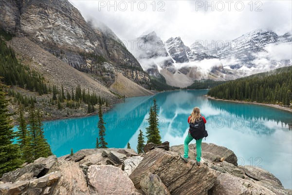 Young woman standing in front of a lake looking into mountain scenery