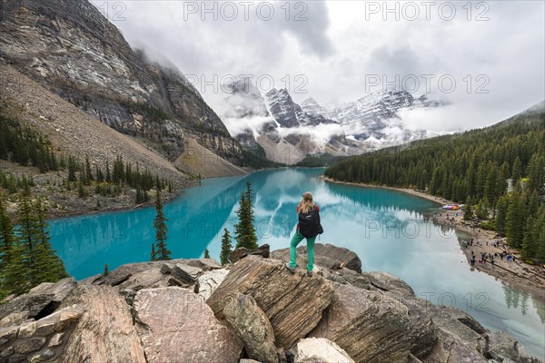 Young woman standing in front of a lake looking into mountain scenery