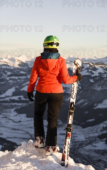 Female skier with ski helmet stands with ski at the ski slope over the valley