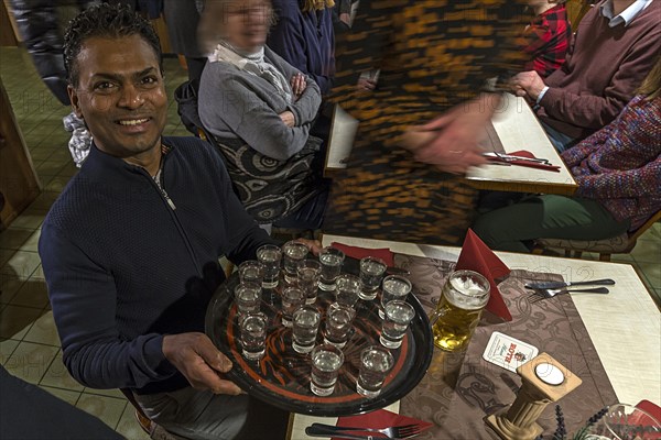 Waiter holds a tray of full Ouzoglasses in a restaurant