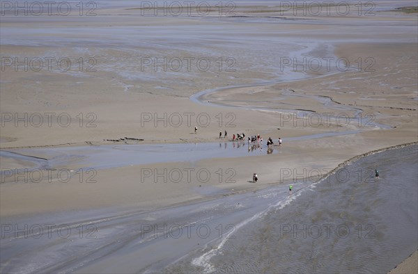 Hikers in mudflat at low tide in Mont Saint Michel