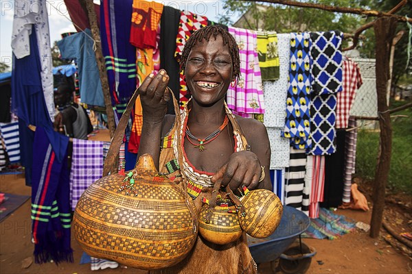 Laughing woman of the Hamer ethnic group sells artfully decorated calabashe pumpkins