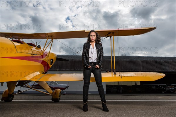 Young woman with leather jacket poses with yellow double-decker aviator