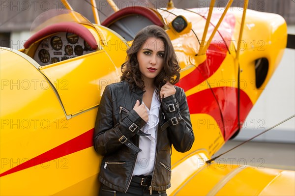 Young woman with leather jacket poses with yellow double-decker aviator