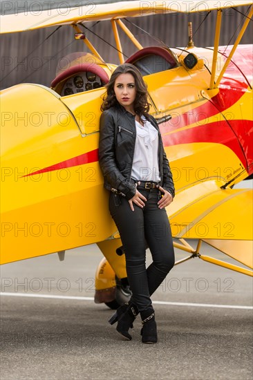 Young woman with leather jacket poses with yellow double-decker aviator