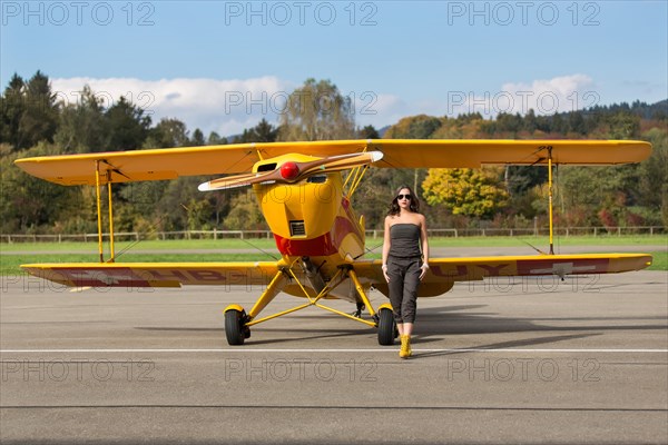 Young woman with sunglasses in overall and boots posing in front of double-decker airplane