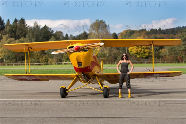 Young woman with sunglasses in overall and boots posing in front of double-decker airplane