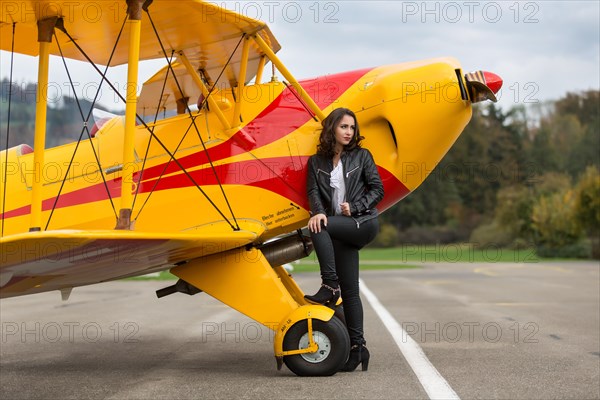 Young woman with leather jacket poses with yellow double-decker aviator