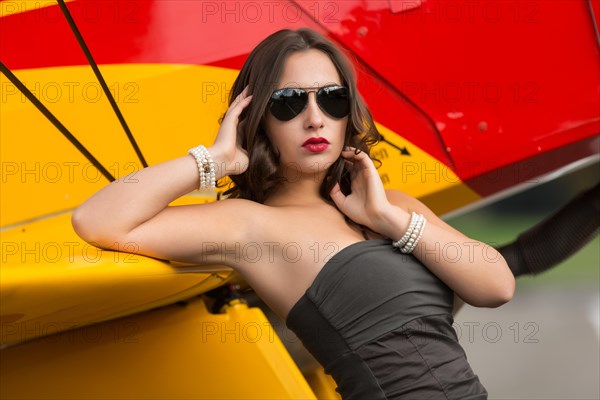 Young woman with sunglasses in overall and boots posing in front of double-decker airplane