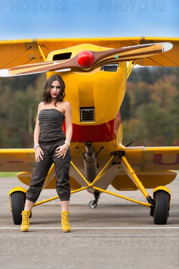 Young woman with sunglasses in overall and boots posing in front of double-decker airplane