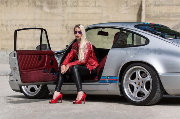 Young woman with long blonde hair poses with Porsche 911 Carrera 4