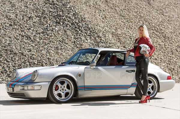 Young woman with long blonde hair poses with Porsche 911 Carrera 4