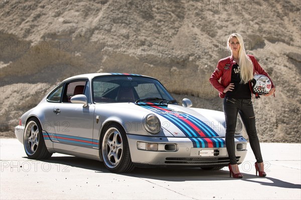 Young woman with long blonde hair poses with Porsche 911 Carrera 4