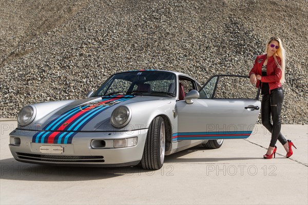 Young woman with long blonde hair poses with Porsche 911 Carrera 4