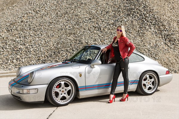 Young woman with long blonde hair poses with Porsche 911 Carrera 4