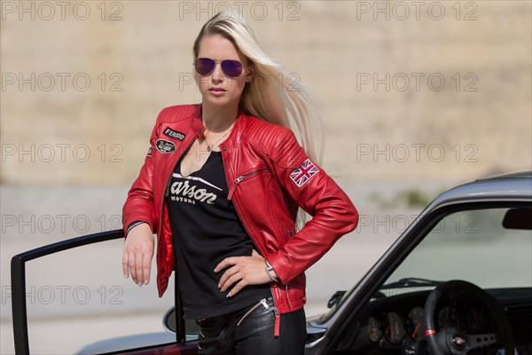 Young woman with long blonde hair poses with Porsche 911 Carrera 4