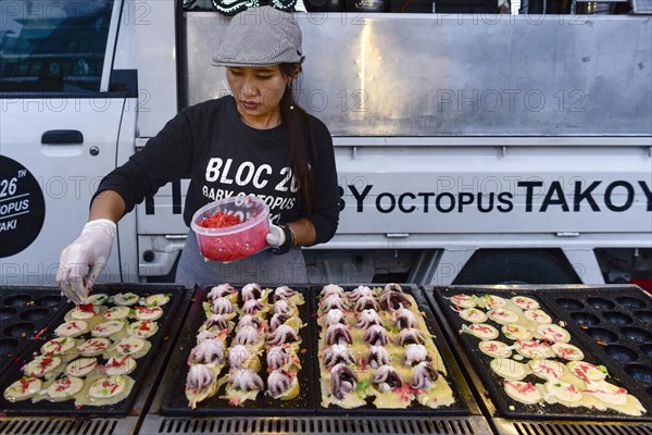 Woman sells baby octopus from grill at a food stall