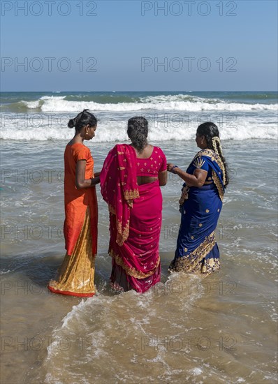 Three women in sari dress stand in ocean on the Bay of Bengal coast