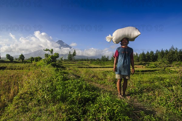 Man with bag of rice on his head before volcano Mayon