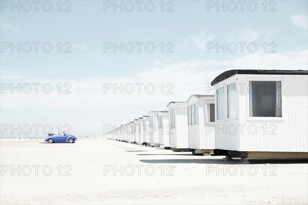 Blue VW Beetle cabriolet faces white beach huts