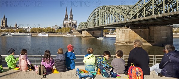 Children's group having a picnic on the Rhine Boulevard with Cologne Cathedral and Hohenzollern Bridge in the background