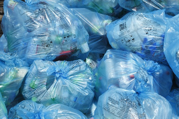 Full light blue garbage bags with plastic garbage on one heap