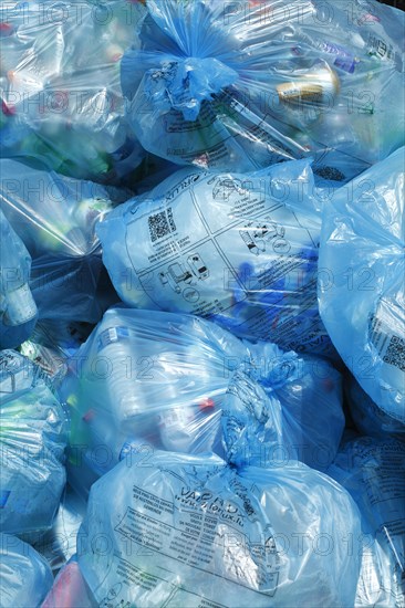 Full light blue garbage bags with plastic garbage on one heap