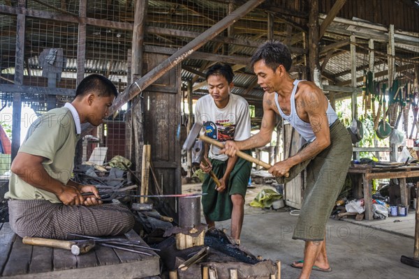 Local blacksmiths banging with hammers on glowing piece of metal