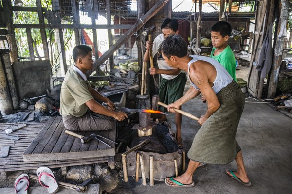 Local blacksmiths banging with hammers on glowing piece of metal