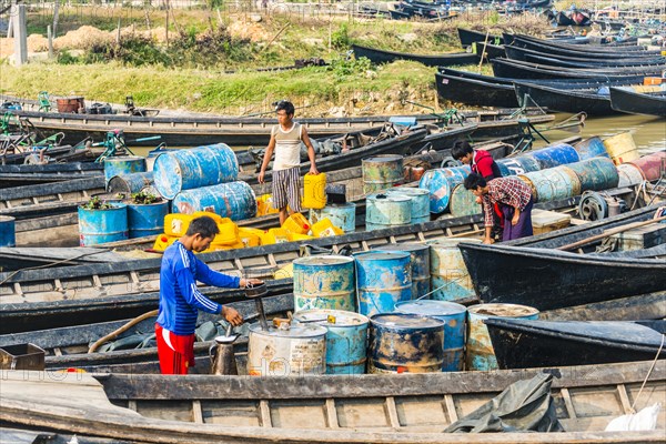 Men working in wooden boats with old oil barrels in the harbor