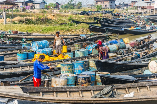 Men working in wooden boats with old oil barrels in the harbor