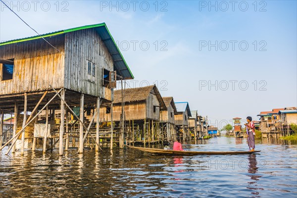 Wooden boat with locals in front of traditional stilt houses on Inle Lake