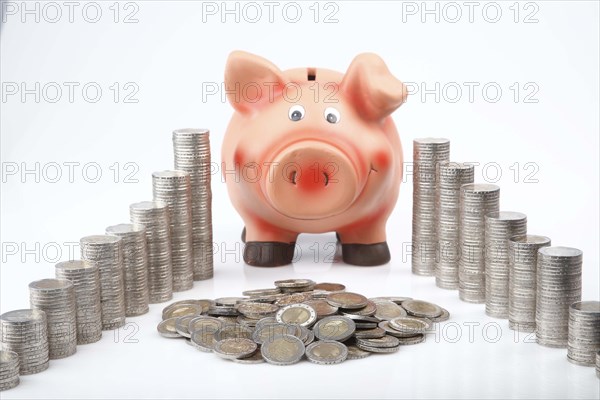 Piggy bank behind heaped and stacked coins