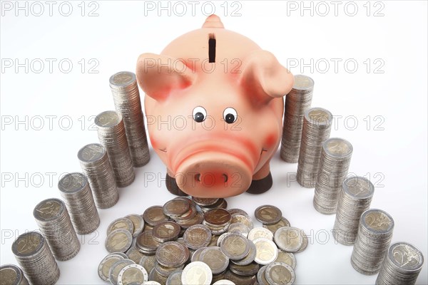 Piggy bank behind heaped and stacked euro coins