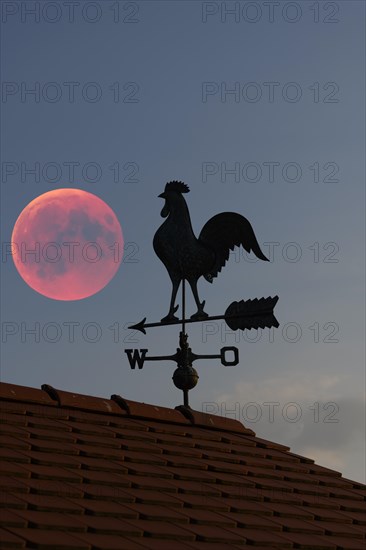 Blood moon over the roof of a house with weather vane with weather cock