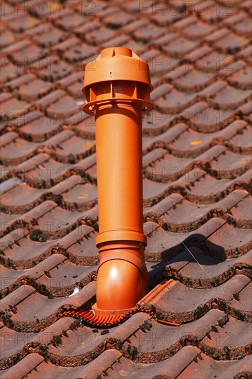Red chimney made of plastic on a tile roof