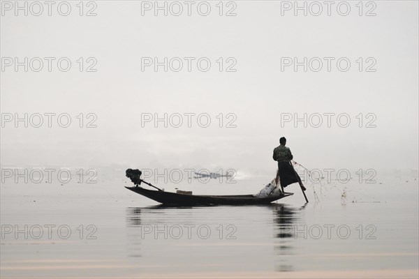 Local fisherman leg rower with wooden boat in the morning fog