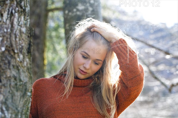 Young girl with long blond hair leaning on a tree