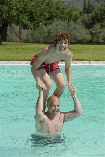 Teenage boy standing on his father's shoulders in a swimming pool