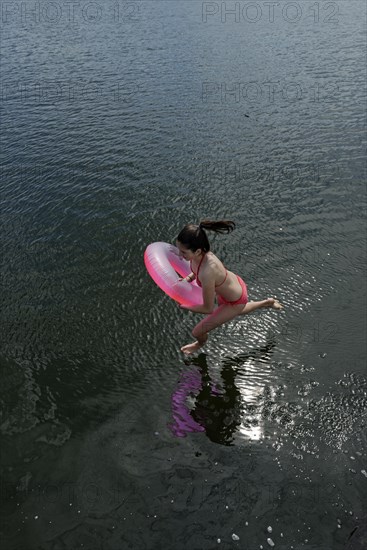 Girl with pink floating tire jumps into the water