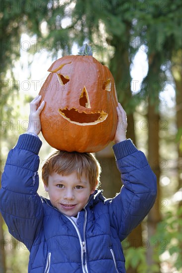 Boy balancing a Halloween pumpkin on his head in autumn