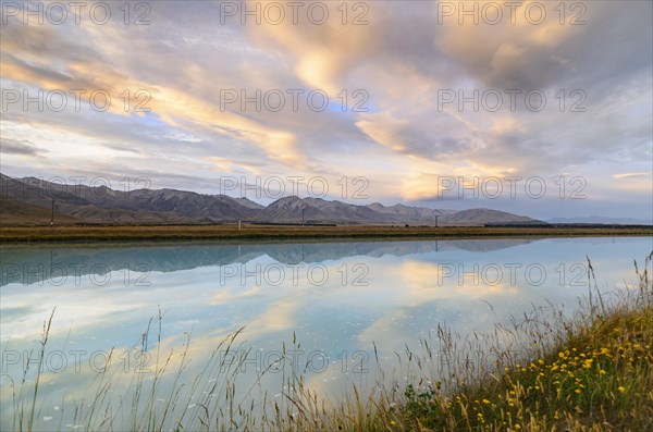 Mountains of the Southern Alps reflected in Tekapo Canal with cloudy sky