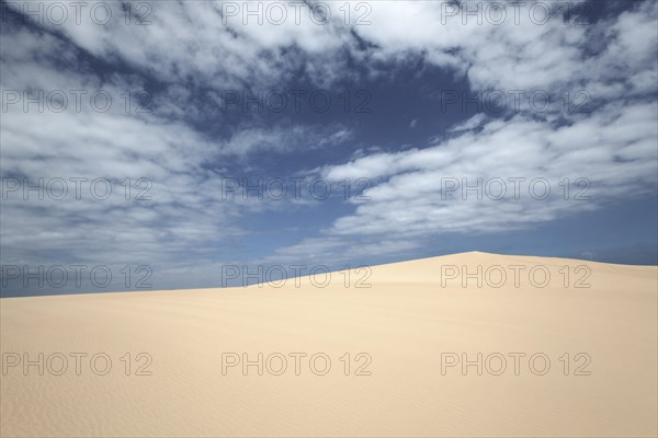 Sand dunes under blue sky with clouds