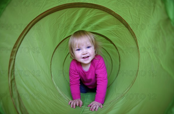 Little girl with pink shirt crawling through green playing tunnel