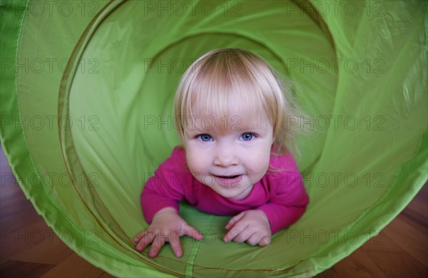 Little girl with pink shirt crawling through green playing tunnel